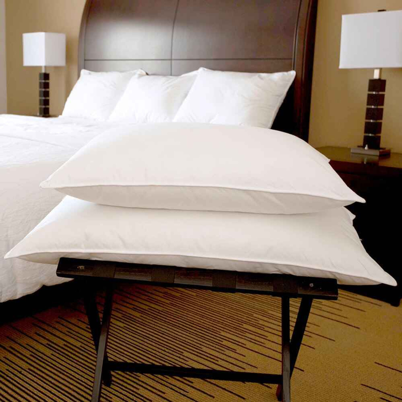 Two pillows stacked on luggage rack in foreground, in background a warm toned room decor